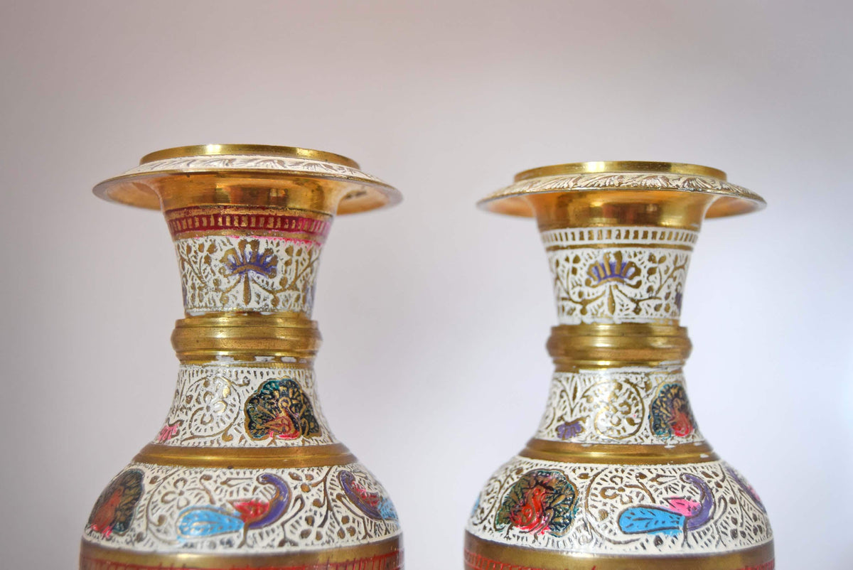 A pair of ornate traditional Indian brass vases with intricate hand-painted motifs and gold-plated rims, set against a plain light gray background.