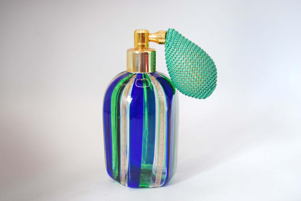 A vintage-style glass perfume atomizer bottle with vertical blue, green, and clear glass stripes, a gold-tone metal pump, and a green mesh-covered bulb, shown on a light gray background.