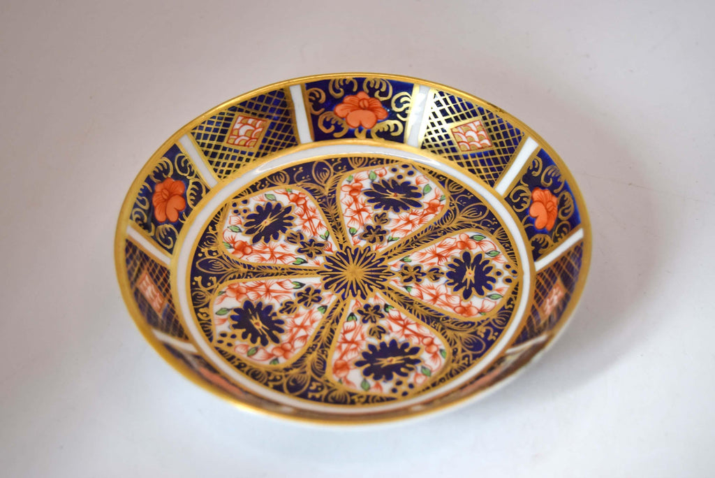 Royal Crown Derby fine bone china small pin dish (trinket dish/butter pat) in the iconic Old Imari 1128 pattern. This piece features the famous rich cobalt blue, iron-red floral motifs, and hand-applied 22-karat gold gilding.