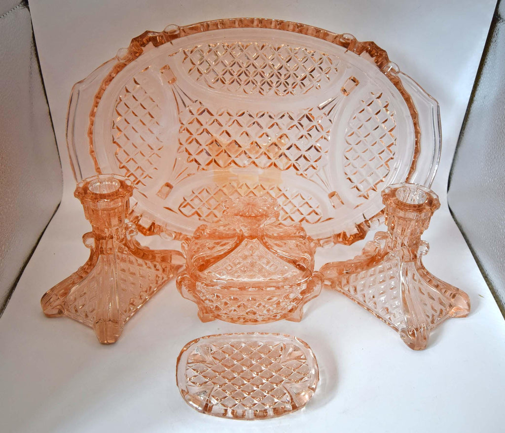 A pink cut-glass table setting with an oval platter, two candlesticks, a small bowl, and a matching tray, displayed on a white background.