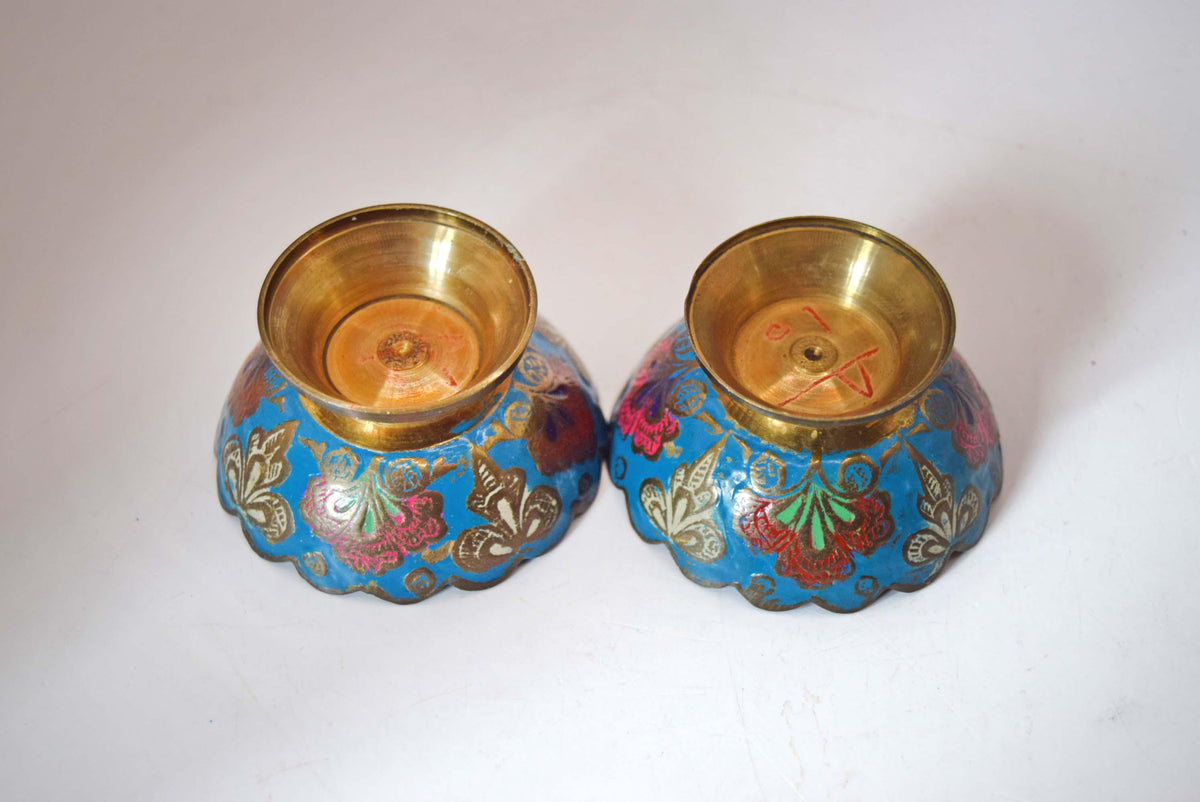 vintage solid brass pedestal bowls featuring vibrant hand-painted Champlevé-style enamel work.
The interior and exterior of each bowl showcase an intricate floral and leaf pattern set against a brilliant turquoise-blue enamel background. The design is framed by a distinct, hand-etched scalloped rim and elevated on a classic flared brass base.
