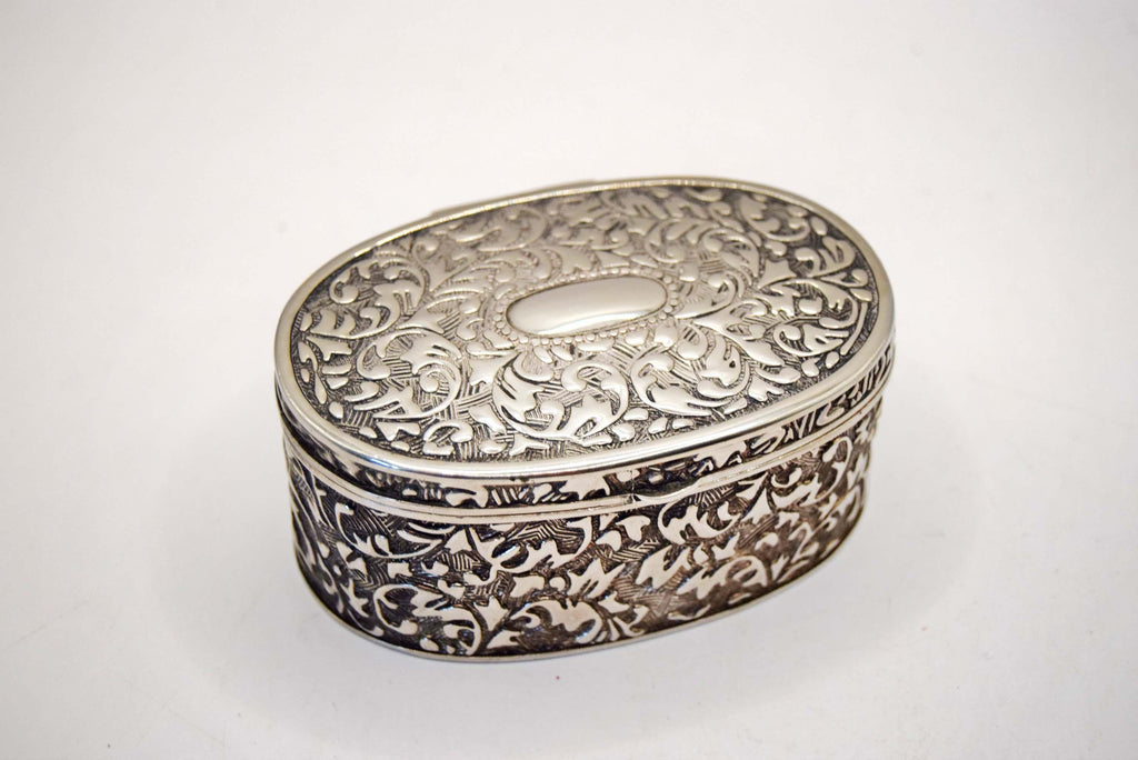 An ornate oval silver box with intricate floral engravings on the lid and sides, photographed on a plain white background.
