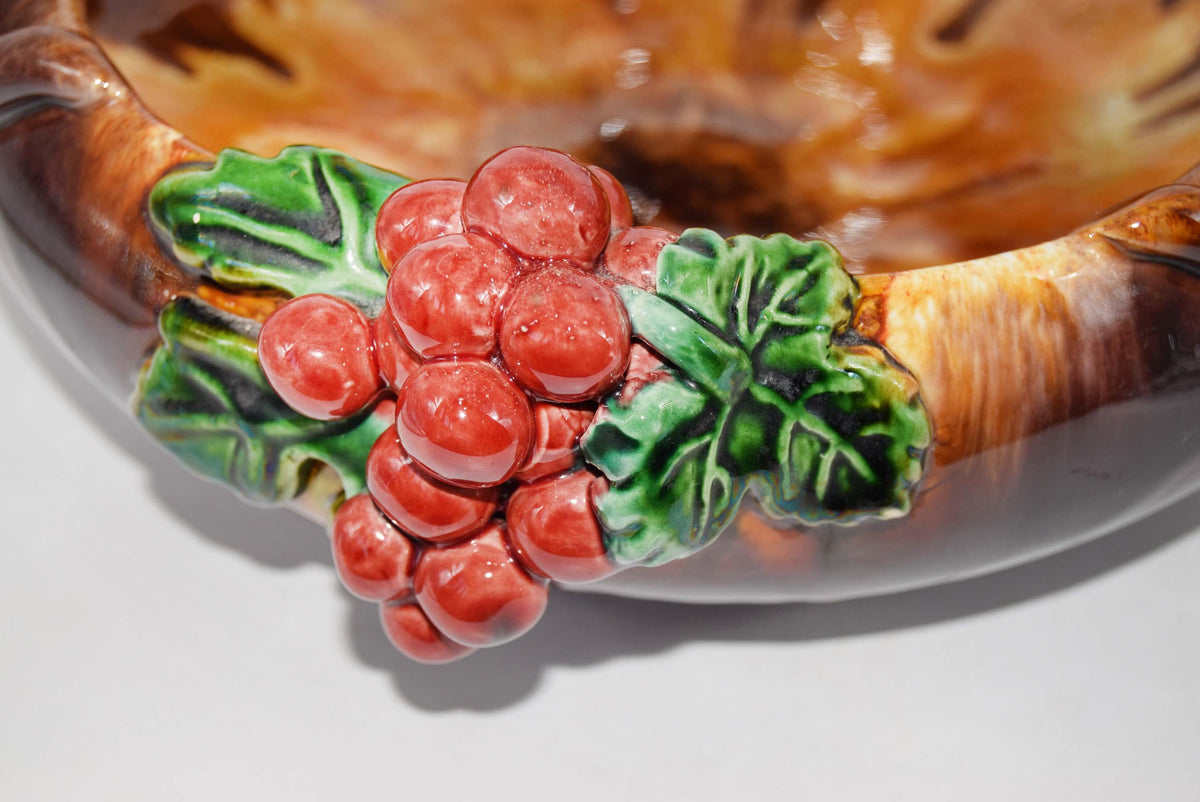 Close-up of a glossy ceramic bowl featuring a raised decorative cluster of red berries with green leaves on the rim, set against a warm brown marbled background.