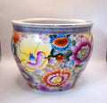 A round ceramic planter pot decorated with a vibrant, hand-painted floral pattern featuring pink, orange, blue, and yellow flowers on a white background, with a blue patterned band around the rim.