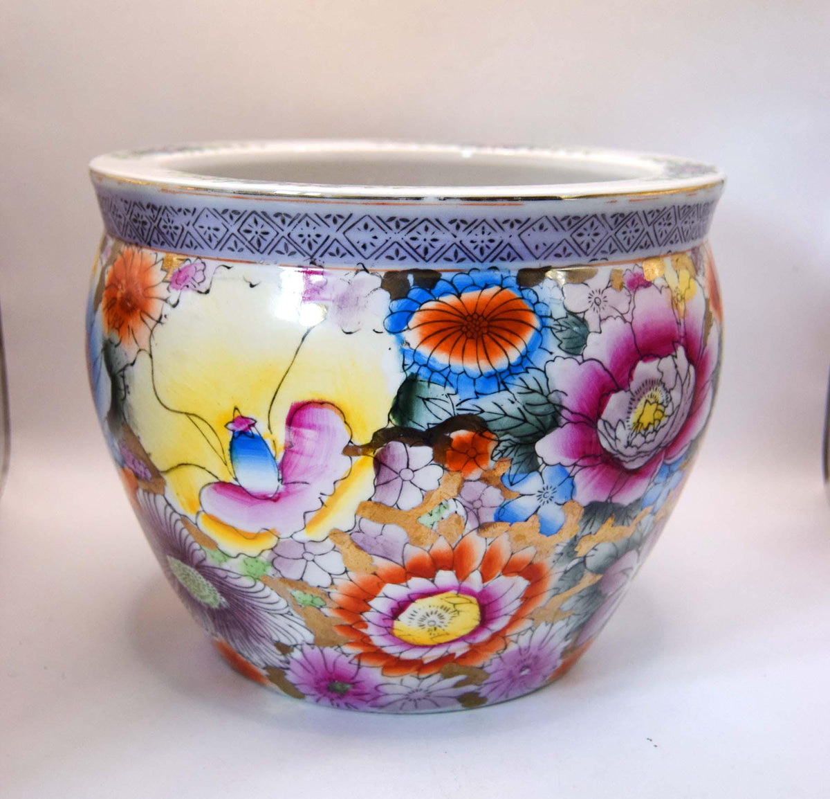 A round ceramic planter pot decorated with a vibrant, hand-painted floral pattern featuring pink, orange, blue, and yellow flowers on a white background, with a blue patterned band around the rim.