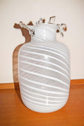 A white glass vase with horizontal ridges and flared glass necks, displayed on a wooden surface against a plain light background.