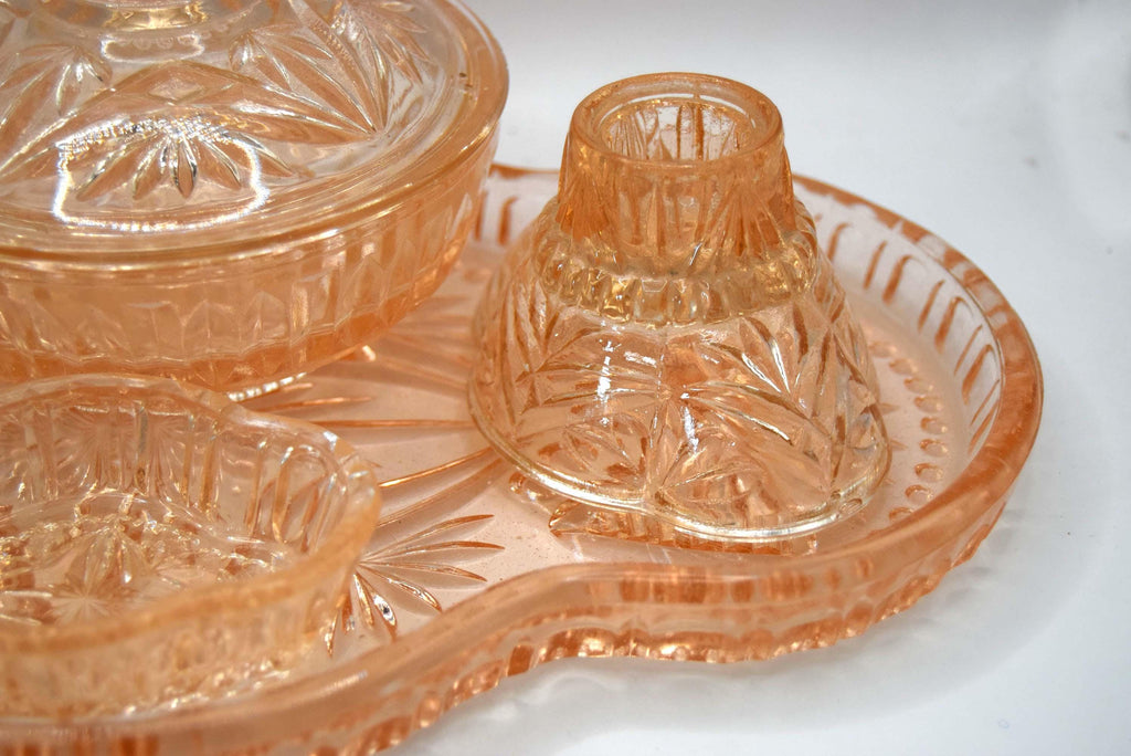 This 1930s–1940s Hollywood Regency Art Deco vanity set is crafted from heavy peach-pink depression glass featuring a geometric starburst and radial fan pattern.