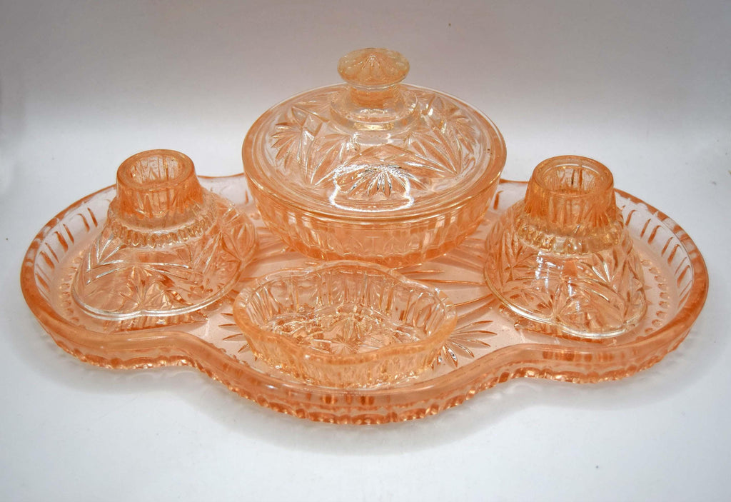 This 1930s–1940s Hollywood Regency Art Deco vanity set is crafted from heavy peach-pink depression glass featuring a geometric starburst and radial fan pattern.