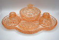 This 1930s–1940s Hollywood Regency Art Deco vanity set is crafted from heavy peach-pink depression glass featuring a geometric starburst and radial fan pattern.