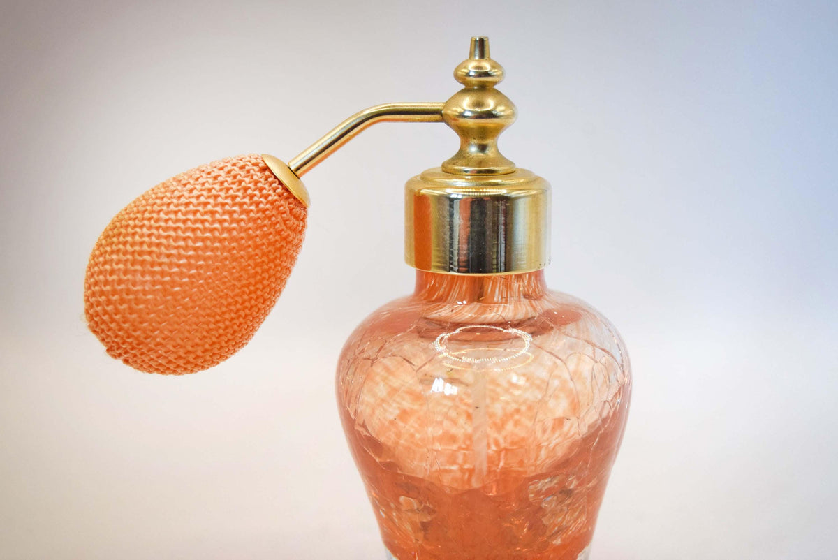 A vintage-style perfume atomizer with a textured orange glass bottle, a brass pump collar, and an orange mesh bulb, shown against a light gray background.
