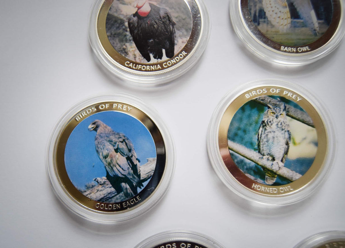 A set of round bird-themed collectible coins or medallions in clear plastic cases, featuring images of California condor, barn owl, golden eagle, and horned owl with gold-rimmed borders and bird names printed below each illustration.