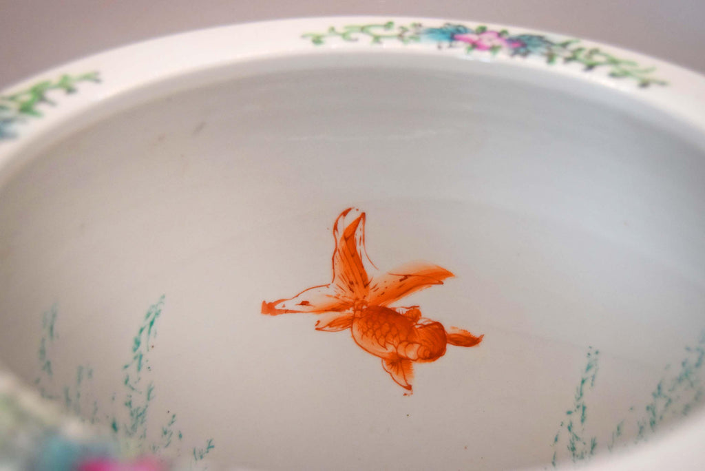 A close-up view inside a white ceramic bowl decorated with a colorful floral rim and delicate green and pink painted details, featuring a small orange fish illustration in the center.