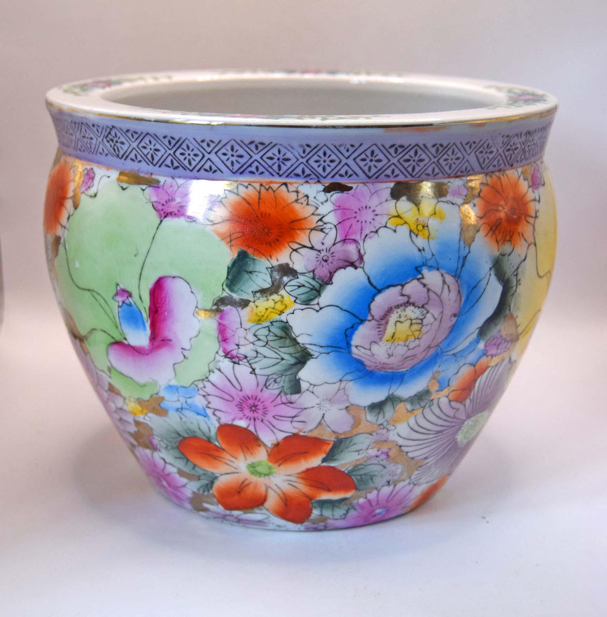 A round ceramic planter pot decorated with a vibrant, multicolored floral pattern in the style of Chinese Famille Rose porcelain, featuring a blue patterned band around the rim.
